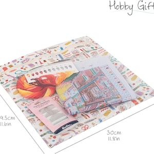 May include: A white fabric bag with a colorful pattern of sewing supplies, including needles, thread, scissors, and buttons. The bag contains a cross-stitch kit with a printed design and a pack of needles. The bag measures 11.8 inches by 11.6 inches.