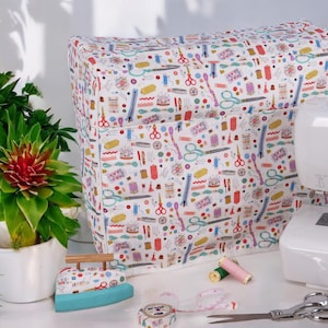 Peut inclure: Une housse de machine à coudre blanche avec un motif coloré d'illustrations sur le thème de la couture, notamment des ciseaux, des bobines de fil, des boutons et des aiguilles. La housse est en tissu et possède une fermeture éclair.