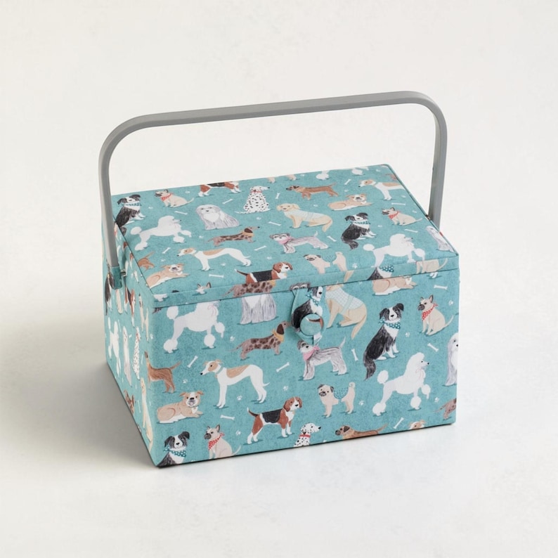 May include: A rectangular sewing basket with a teal fabric exterior featuring a repeating pattern of various dog breeds in multiple colors. The basket includes a solid gray plastic handle and a fabric-covered button closure on the front lid.