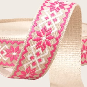 May include: A beige ribbon with a pink and white geometric pattern. The ribbon is woven with a repeating design of flowers and diamonds.