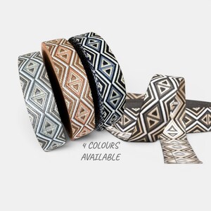 Peut inclure: Quatre rouleaux de tissu à motifs dans les tons de gris, marron et bleu marine. Chaque rouleau présente un motif géométrique en losanges. Le texte "4 COULEURS DISPONIBLES" est visible en dessous.