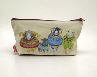 May include: A cream-colored zippered pouch featuring a watercolor illustration of four sheep wearing colorful patterned sweaters. The sheep are depicted in shades of red, blue, green, and yellow. A small red tag on the side reads Emma Ball.