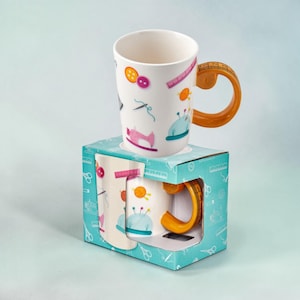 Könnte beinhalten: Ein Set aus drei Keramikbechern mit gesprenkelter, matter Oberfläche. Die Becher sind in Creme-, Hellgrau- und Dunkelgrautönen gehalten. Jeder Becher hat ein schlichtes, minimalistisches Design und einen abgerundeten Henkel.