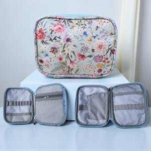 May include: A floral print cosmetic bag with a light blue zipper and trim. The bag is open, revealing several compartments and pockets. The bag is decorated with a pattern of pink, red, and purple flowers.