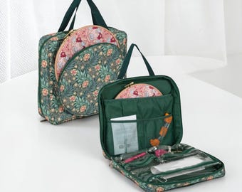 May include: Two green floral print craft bags with dark green handles. One bag is open, revealing a pink floral embroidery hoop and various craft supplies. The other bag is closed, with a matching pink floral embroidery hoop visible.