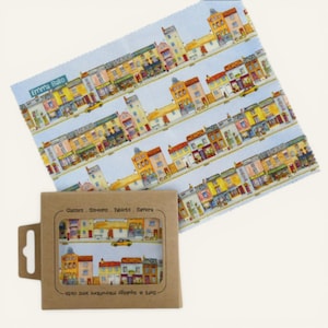 May include: A light blue microfiber lens cloth and packaging featuring a colorful illustration of a street with buildings. The cloth has the text "Emma Ballo". The packaging reads "Glasses, Screens, Tablets, Camera" and "Soft & squidgy microfiber lens cloth."