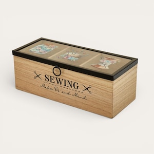 May include: A rectangular wooden sewing box with a black framed glass lid. The lid is divided into three sections, each with a sewing-themed illustration. The box has the text "SEWING Make Do and Mend" printed on the front.