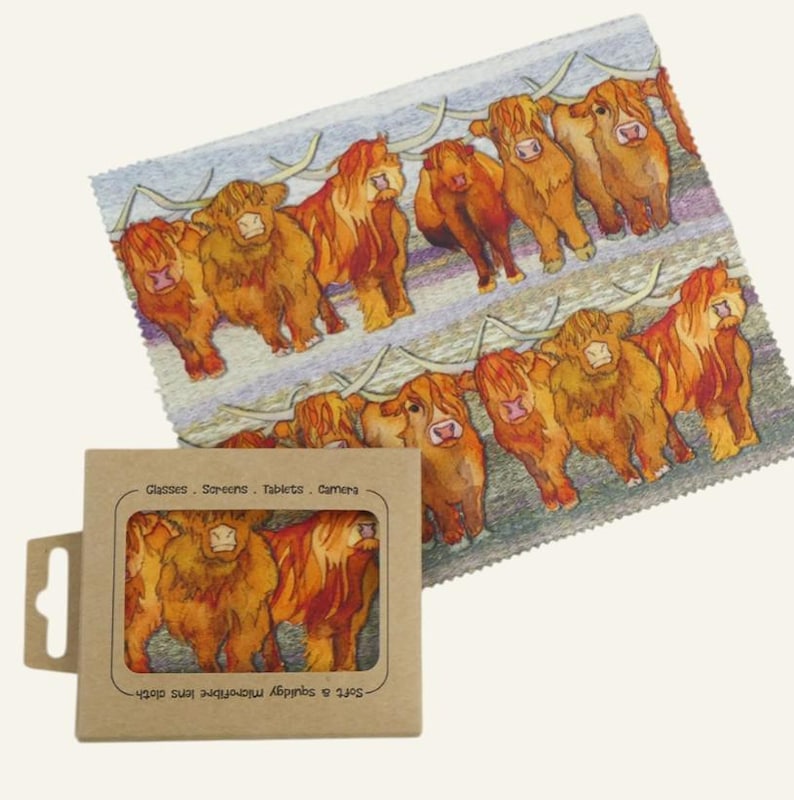 May include: A microfiber lens cloth with a repeating pattern of Highland cows in shades of brown and orange. The cloth is accompanied by a cardboard box with a matching cow design. The box has text that reads "Glasses. Screens. Tablets. Camera."