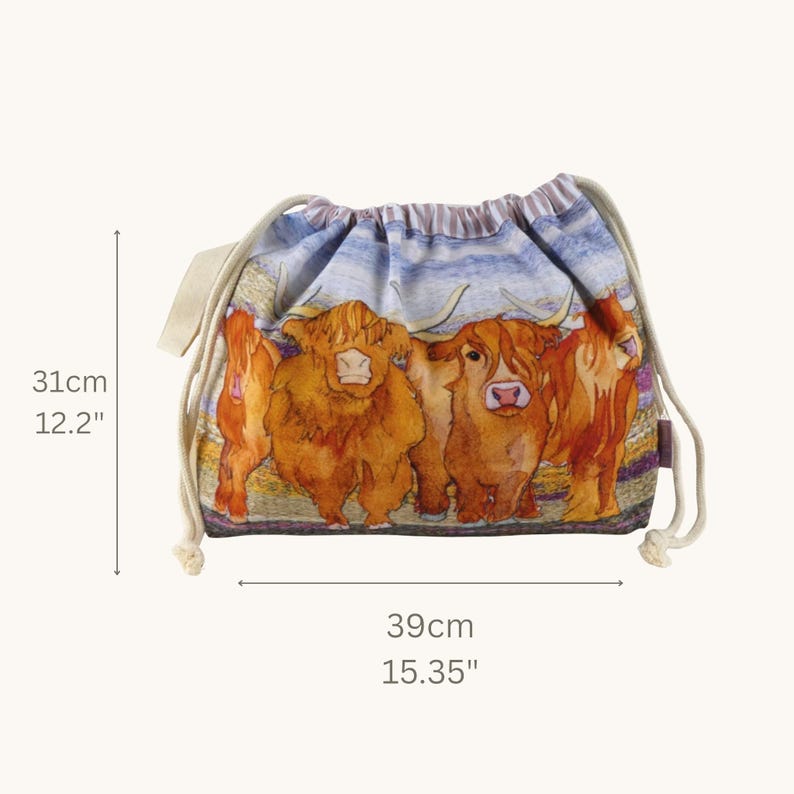 Op de afbeelding: Een tas met trekkoord voorzien van een kleurrijke illustratie van drie Schotse hooglanders tegen een blauwe lucht. De tas is 31 cm hoog en 39 cm breed, met cr&egrave;mekleurige koordhengsels en een gestreepte stoffen bovenrand.