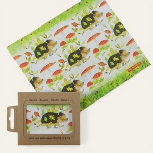 May include: A soft, squiggly microfiber lens cloth with a repeating pattern of cartoon hedgehogs, red mushrooms, and leaves. The cloth is white with green borders and comes in a brown cardboard box. The box has the text: "Glasses, Screens, Tablets, Cameras."