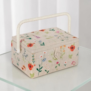 Pode incluir: Uma caixa de costura retangular com exterior em tecido bege tipo linho, apresentando flores silvestres, papoulas e pequenas borboletas bordadas em vermelho, laranja, rosa e azul. Inclui uma alça trançada branca e fecho de botão.
