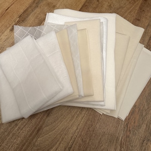 May include: A stack of white and cream fabric swatches. The fabric is smooth and has a subtle sheen.