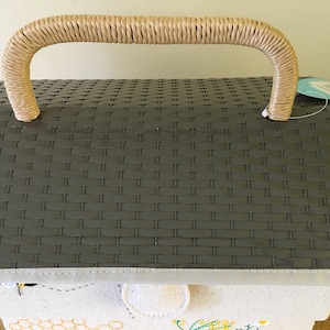 May include: A gray picnic basket with a woven pattern on the lid and a beige woven handle. The basket has a light-colored trim and a fabric base with embroidered bee and honeycomb designs. A tag hangs from the side.