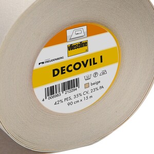 May include: A roll of beige Decovil I interfacing for sewing projects. The label reads "Decovil I" with the brand name "Vlieseline" and a product code of "008983 212294". The label also indicates the fabric composition: 42% PES, 35% CV, 23% PA. The roll is 90 cm x 15 m.
