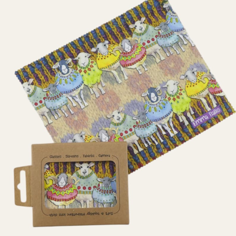May include: A microfiber lens cloth with a colorful sheep design. The cloth features sheep wearing sweaters in various colors, set against a knitted background. A small cardboard box with a window shows a matching design. The text "Emma Ballo" is visible.