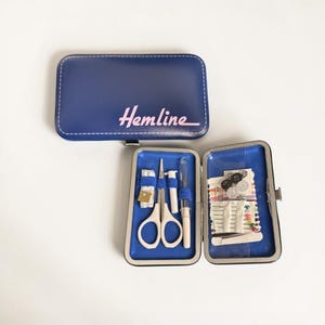 May include: A navy blue sewing kit, branded "Hemline" in pink, open to display sewing essentials. It contains scissors, needles, thread, and buttons. The kit is designed for portability and ease of use, ideal for small repairs.