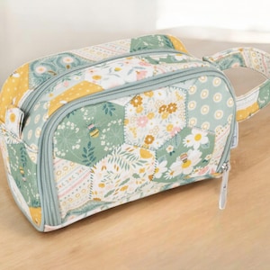 May include: A green, yellow and white patchwork fabric cosmetic bag with a zipper closure and a top handle. The bag has a floral and bee design.