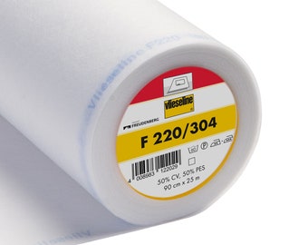 Peut inclure: Un rouleau de tissu non tissé Vlieseline F220 blanc. L'étiquette indique le nom du produit, la marque Freudenberg et les dimensions : 90 cm x 25 m. Le tissu est composé de 50% CV et 50% PES.