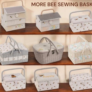 May include: A collection of bee-themed sewing baskets in various shapes and sizes. The baskets feature light colors, floral patterns, and bee motifs. Some have handles, while others have a house-like design. The text "MORE BEE SEWING BASKETS" is visible.