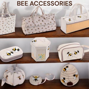 May include: A collection of bee-themed accessories, including tote bags, a travel bag, a cosmetic bag, a sewing kit, a hexagonal storage box, a pincushion, and a tape measure. The items are beige with black and yellow bee designs. The text "BEE ACCESSORIES" is at the top.