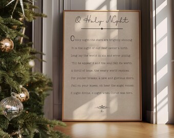 May include: A printable art print with a white background and black text. The text reads "O Holy Night" and includes the lyrics to the Christmas carol. The print is framed in a gold frame and is leaning against a wall with a Christmas tree in the foreground.