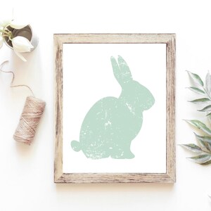 Puede incluir: Una impresi&oacute;n enmarcada de una silueta de conejo verde claro con una textura desgastada. El marco es de madera con un acabado marr&oacute;n claro.