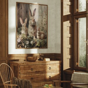 May include: A framed print of three brown rabbits in a forest setting. The rabbits are surrounded by green leaves and flowers. The print is in a wooden frame and is hanging on a wall.