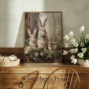 May include: A vintage-style illustration of three brown rabbits in a field of flowers. The rabbits are sitting in a grassy area with a wooden fence in the background. The image is framed in a brown wooden frame.