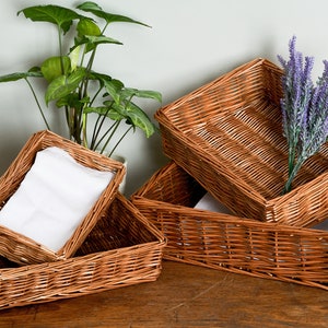 May include: Four brown wicker baskets stacked on top of each other. The top basket contains a bouquet of purple lavender flowers. The second basket has a white cloth napkin inside. The bottom two baskets are empty.