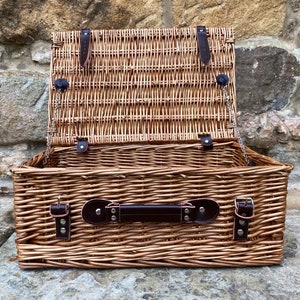 May include: A brown wicker picnic basket with a leather handle and clasps. The lid is open and the basket is empty.