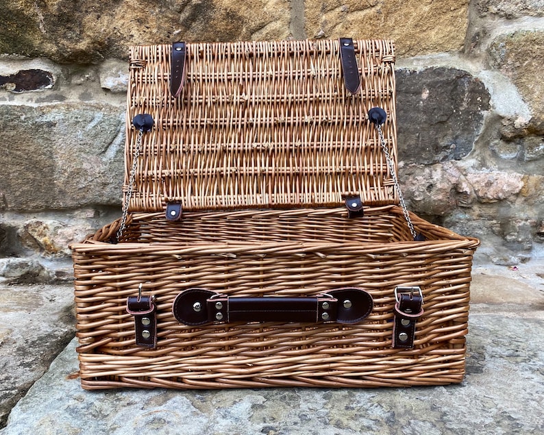 May include: A brown wicker picnic basket with a leather handle and clasps. The lid is open and the basket is empty.