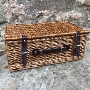 May include: A woven wicker basket with a brown leather handle and two leather straps with buckles. The basket is closed and has a natural brown color.