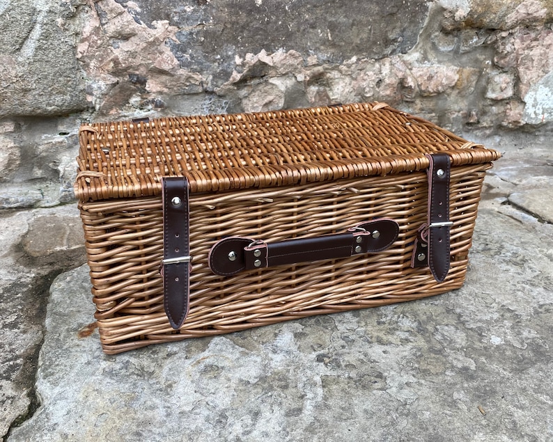 May include: A woven wicker basket with a brown leather handle and two leather straps with buckles. The basket is closed and has a natural brown color.