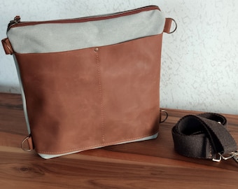 Puede incluir: Un bolso bandolera de lona azul claro y cuero marrón con una correa ajustable marrón oscuro. El bolso tiene cierre de cremallera y una solapa con cierre de presión.