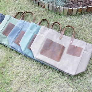 K&ouml;nnte beinhalten: F&uuml;nf Canvas-Tragetaschen mit Lederelementen. Die Taschen sind in einer Reihe angeordnet, wobei die gr&ouml;&szlig;te Tasche vorne und die kleinste Tasche hinten ist. Die Taschen sind alle in verschiedenen Farben, darunter Grau, Blau, Gr&uuml;n und Beige.