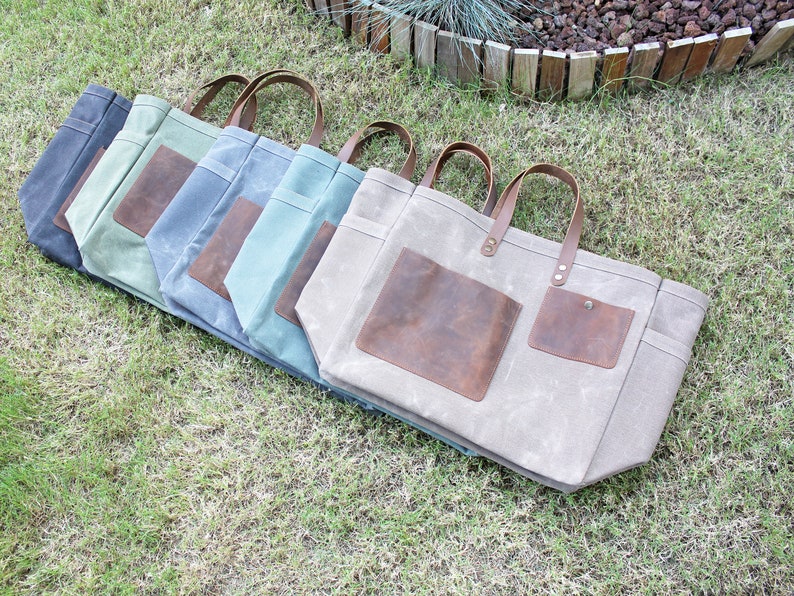 K&ouml;nnte beinhalten: F&uuml;nf Canvas-Tragetaschen mit Lederelementen. Die Taschen sind in einer Reihe angeordnet, wobei die gr&ouml;&szlig;te Tasche vorne und die kleinste Tasche hinten ist. Die Taschen sind alle in verschiedenen Farben, darunter Grau, Blau, Gr&uuml;n und Beige.