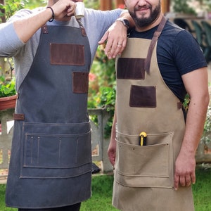 Op de afbeelding: Twee mensen dragen bruine leren en canvas schorten met meerdere zakken. De schort links is donkergrijs en de schort rechts is beige.