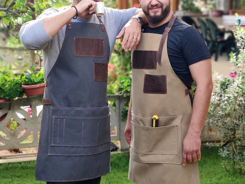 Op de afbeelding: Twee mensen dragen bruine leren en canvas schorten met meerdere zakken. De schort links is donkergrijs en de schort rechts is beige.