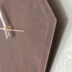 May include: A brown leather hexagon-shaped clock with white stitching around the edges. The clock has white hands and a gold centre.