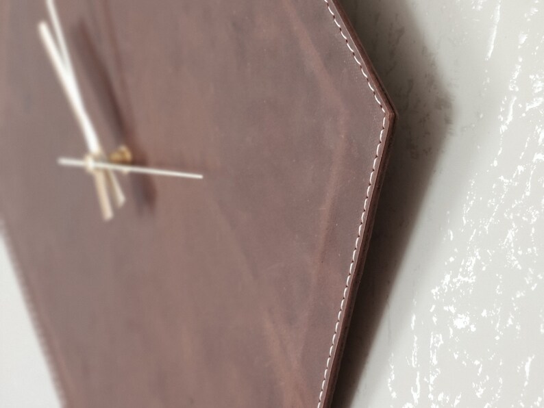 May include: A brown leather hexagon-shaped clock with white stitching around the edges. The clock has white hands and a gold centre.