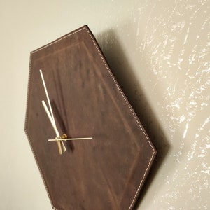 May include: A brown leather hexagon-shaped wall clock with gold-coloured hands.