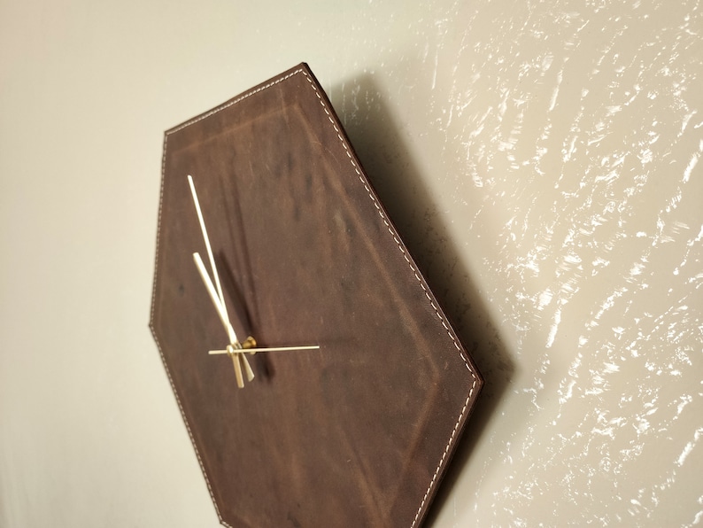 May include: A brown leather hexagon-shaped wall clock with gold-coloured hands.