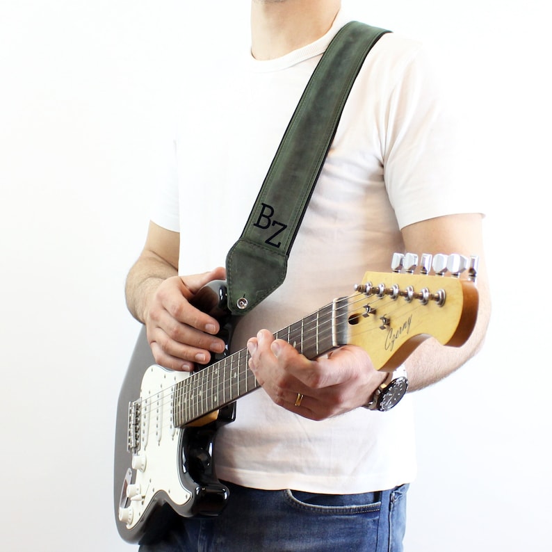 May include: A person playing a guitar with a green leather guitar strap with the initials "BZ" embroidered on it.