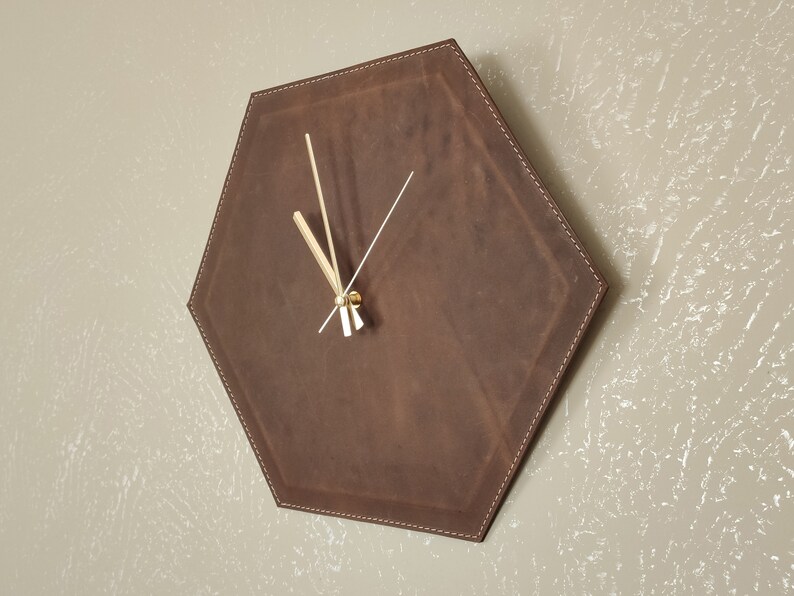 May include: A brown leather hexagon-shaped wall clock with gold-coloured hands.