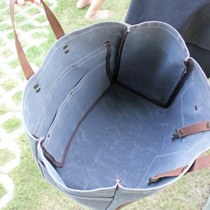 K&ouml;nnte beinhalten: Eine blaue Canvas-Tragetasche mit braunen Lederriemen und Griffen. Die Tasche hat einen gro&szlig;en Innenraum und eine kleinere Tasche auf der Vorderseite.