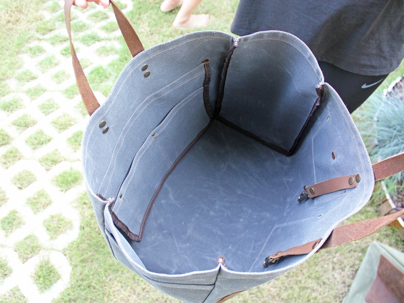 K&ouml;nnte beinhalten: Eine blaue Canvas-Tragetasche mit braunen Lederriemen und Griffen. Die Tasche hat einen gro&szlig;en Innenraum und eine kleinere Tasche auf der Vorderseite.