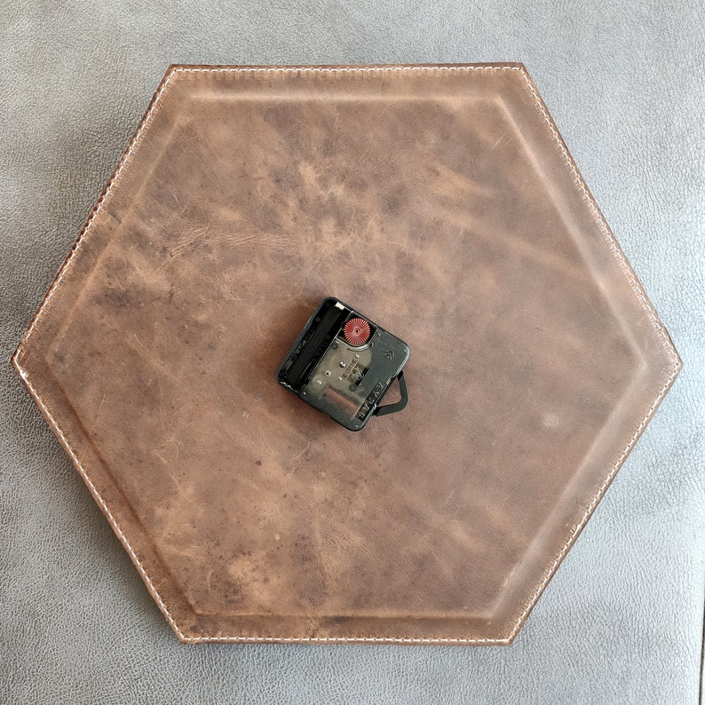 May include: A brown leather hexagon-shaped clock face with a black clock mechanism in the centre.