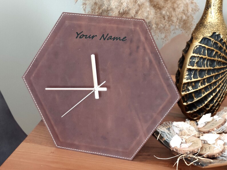 May include: A brown leather hexagon-shaped clock with white hands and the text "Your Name" in black lettering.