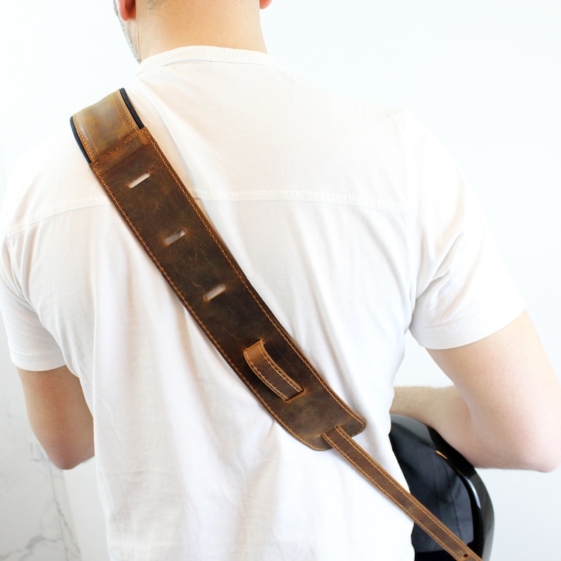 May include: A brown leather guitar strap with adjustable length and a dark brown leather strap with stitching.