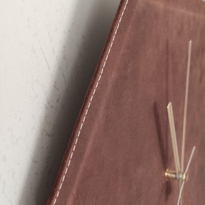 May include: A brown leather clock with white stitching around the edges. The clock face is a hexagon shape and has gold hands.